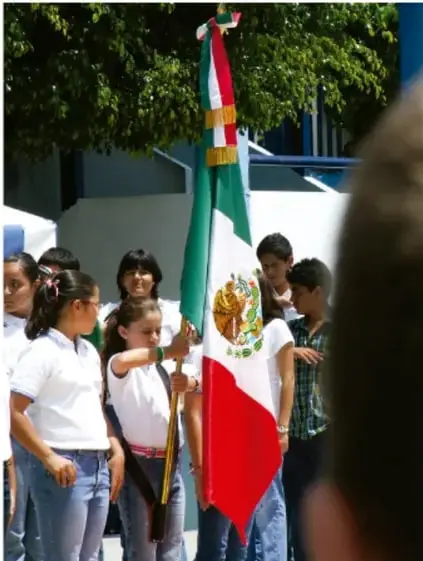 Fotografía de estudiantes en formación escolar sosteniendo la bandera de México durante un acto cívico, ilustrando la identidad nacional.