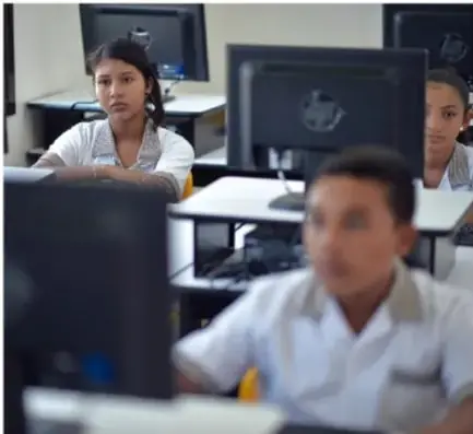 Estudiantes en un aula de computación usando equipos de escritorio.
