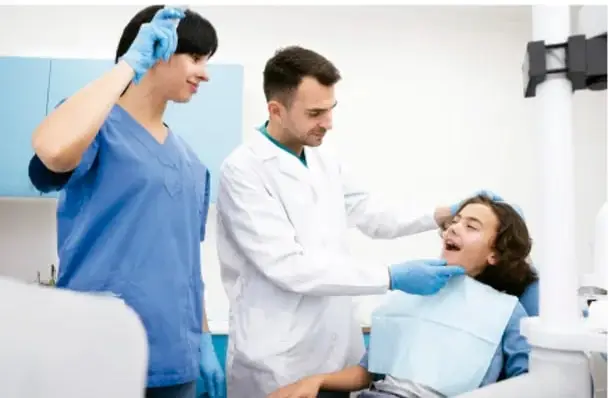 Fotografía de un consultorio dental donde dos profesionales de la salud atienden a una paciente adolescente sentada en el sillón dental.