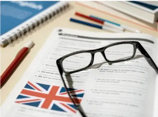 Escritorio con cuaderno, lentes, plumas y una bandera del Reino Unido, junto a un libro de inglés.