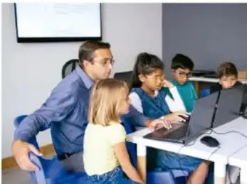 Un docente y varios estudiantes reunidos alrededor de una computadora portátil, trabajando en la digitalización de una infografía.