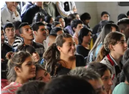 Grupo de jóvenes en un auditorio, algunos levantan la mano.