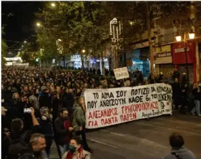 Multitud en una protesta nocturna con pancartas en griego, relacionada con la crisis económica.