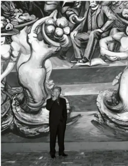 Fotografía en blanco y negro de un hombre de traje frente a un mural monumental con figuras humanas y simbología revolucionaria.