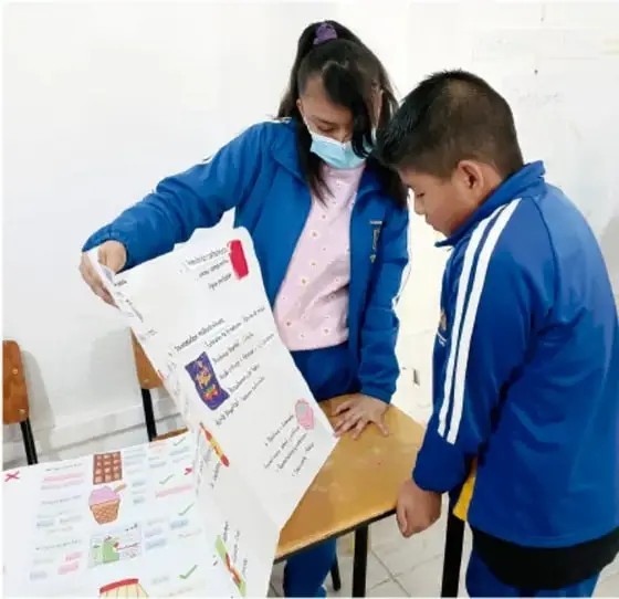 Grupo de estudiantes presentando su periódico mural a dos personas sentadas frente a ellos. Crédito: Luis Eduardo García Medel, Tlaxcala.