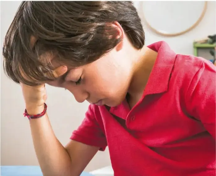 Fotografía de un niño con camisa roja que apoya la cabeza en la mano con los ojos cerrados, ilustrando la técnica de calmarse respirando.
