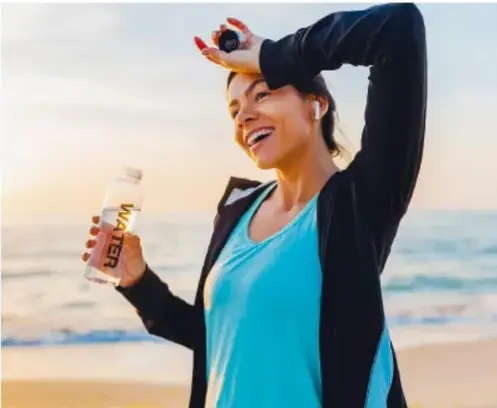 Persona sudando bajo el sol en la playa, sosteniendo una botella de agua, ilustrando temperatura y equilibrio térmico.