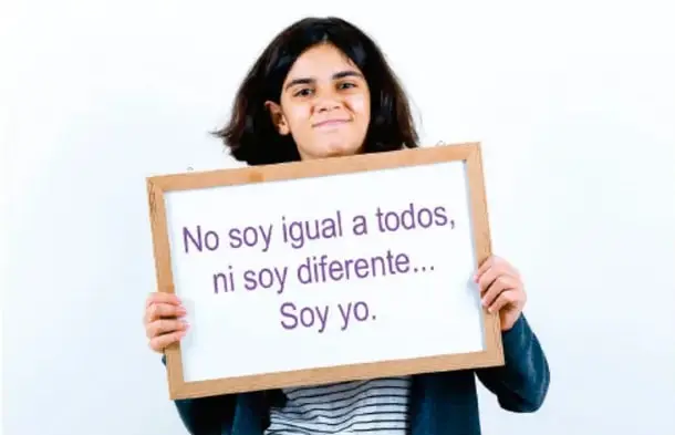Joven sosteniendo un cartel de madera que dice 'No soy igual a todos, ni soy diferente... Soy yo.'