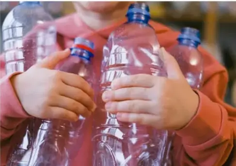 Fotografía de un niño sosteniendo varias botellas de plástico transparentes con tapas azules, ilustrando el material reciclado para el boliche.