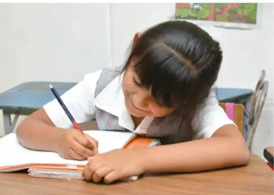 Fotografía de una estudiante de primaria escribiendo en su cuaderno sobre el escritorio.