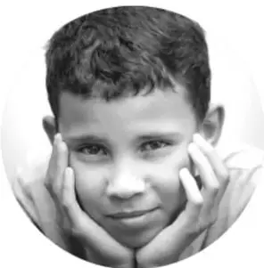 Fotografía en blanco y negro, en óvalo, de un niño sonriendo con las manos apoyadas en el rostro.