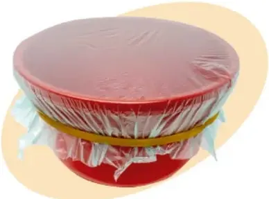 Recipiente de plástico rojo cubierto con plástico transparente y sujeto con una liga amarilla; se observa la tela tensa sobre el recipiente.