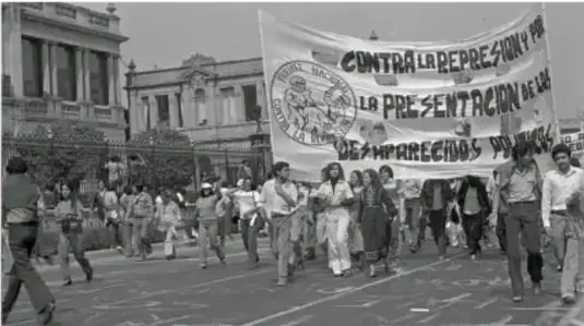Fotografía en blanco y negro de una manifestación callejera en la que participan jóvenes con un gran cartel que dice 'CONTRA LA REPRESIÓN POR LA PRESENTACIÓN DE LOS DESAPARECIDOS'.