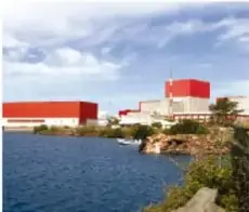Central nuclear junto a un cuerpo de agua, con edificios rojos y grises.