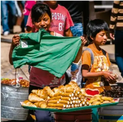 Fotografía de dos jóvenes vendiendo pan y verduras en un puesto callejero, con un cartel que dice 'POSTA' al fondo.