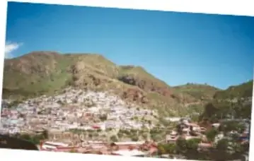Vista actual de la ciudad creciendo hacia las laderas de los cerros, con manchas blancas de viviendas.