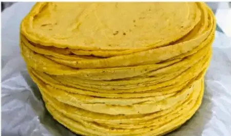 Fotografía de un plato hondo con tortillas de maíz amarillas apiladas sobre papel, ilustrando un alimento tradicional de origen local.