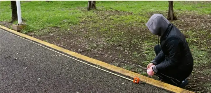 Persona agachada midiendo un ángulo en el suelo con un transportador junto a una línea amarilla.