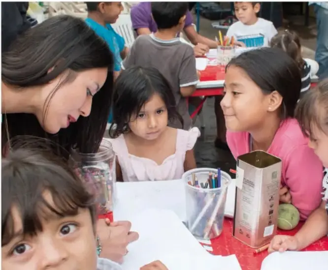 Fotografía de niñas y niños de primaria trabajando en mesas con materiales, conviviendo en el aula.