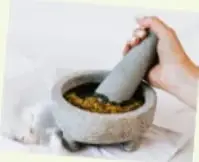 Fotografía de un molcajete de piedra con tejolote y mano moliendo ingredientes.