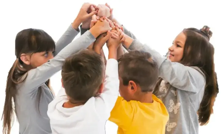 Fotografía de cinco niños y niñas de espaldas que juntan las manos en círculo, como símbolo de comunidad y trabajo en equipo.