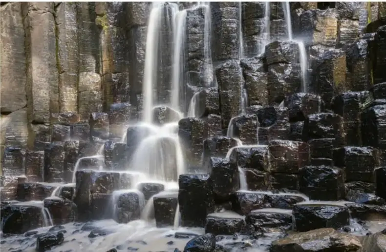 Fotografía de una cascada que cae sobre columnas de roca basáltica.
