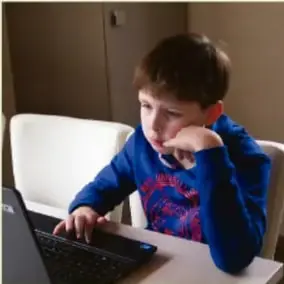 Niño sentado frente a una laptop, ilustrando a un menor expuesto a un adulto desconocido en internet (grooming).