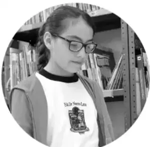 Fotografía de una estudiante con lentes leyendo un libro en una biblioteca.