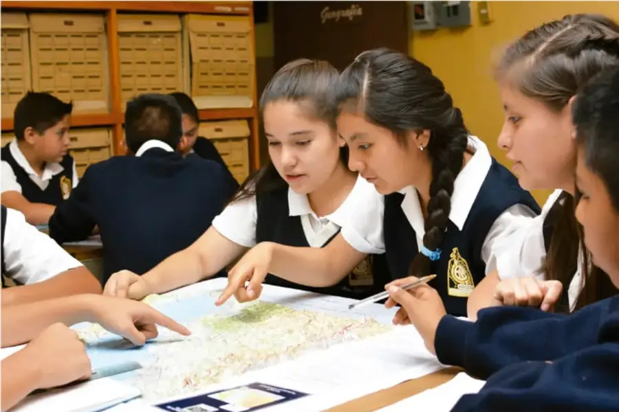 Estudiantes de primaria observando y señalando un mapa sobre una mesa en el aula.