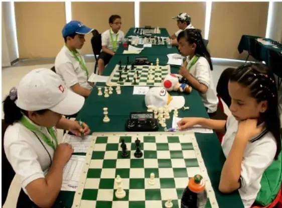 Fotografía de un grupo de niños y niñas de secundaria jugando ajedrez en mesas largas durante una actividad escolar, mostrando concentración y participación conjunta.