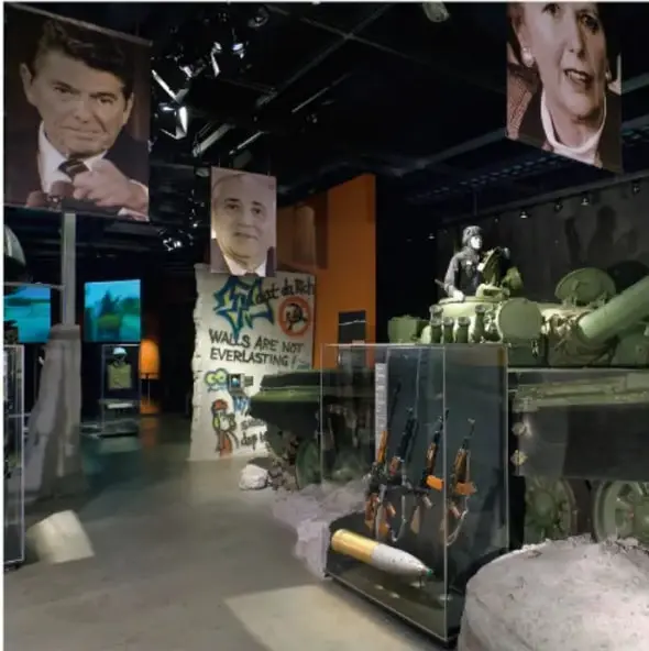 Fotografía de un museo de la Guerra Fría: grandes retratos suspendidos de Ronald Reagan, Mijaíl Gorbachov y Margaret Thatcher; una sección del Muro de Berlín con grafitis ("Walls are not everlasting"); un tanque y armas bajo vitrinas.