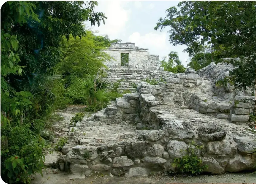 Fotografía de las ruinas de la Pirámide de Xcaret (Polé), rodeada de vegetación, con escalinatas de piedra.
