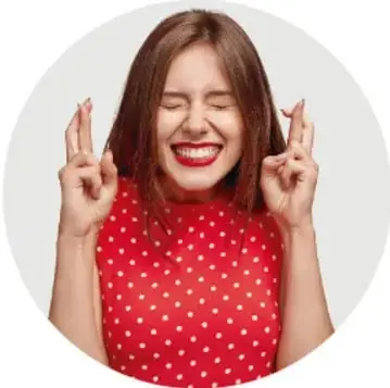 Fotografía de una mujer joven con blusa roja de lunares blancos, guiñando un ojo y con los dedos cruzados en señal de buena suerte.