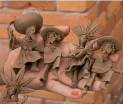 Mano sosteniendo pequeñas figuras de barro sin pintar que representan a músicos con sombrero, junto a una figura con penacho.