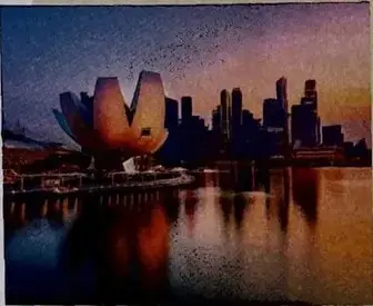 Fotografía panorámica de Singapur al atardecer, con edificios modernos, un cuerpo de agua y el museo ArtScience en primer plano.