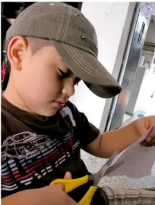 Niño con gorra recortando papel con tijeras.