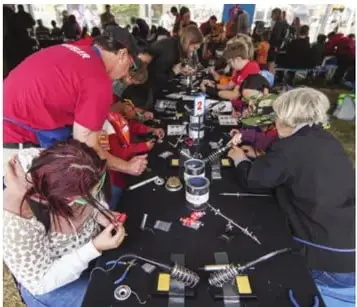 Fotografía de estudiantes en una mesa armando prototipos durante una feria; ilustra el ambiente del taller.