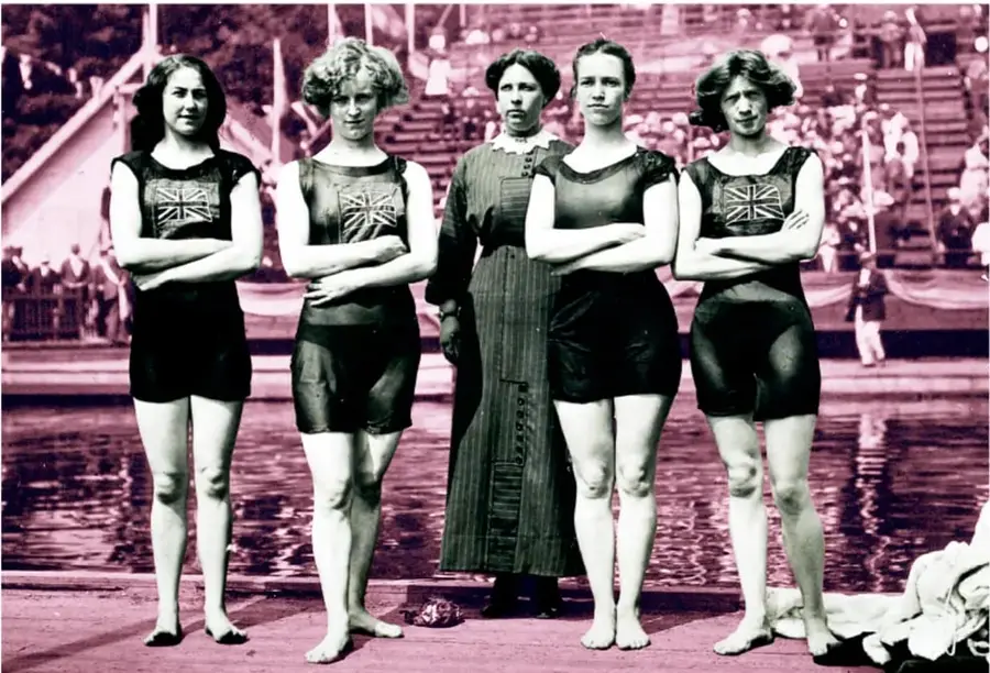 Fotografía histórica con tinte rosa-magenta de cinco nadadoras en trajes de baño de una pieza con la bandera del Reino Unido (Union Jack), de brazos cruzados junto a una alberca; una de ellas viste vestido largo oscuro, con gradas y público al fondo.