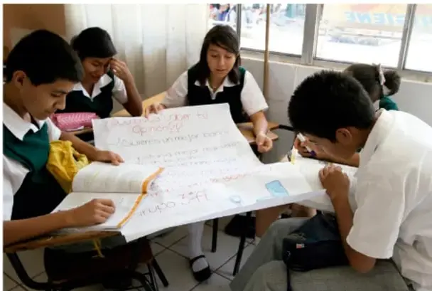 Grupo de estudiantes de telesecundaria trabajando juntos sobre una cartulina grande en el salón de clases.