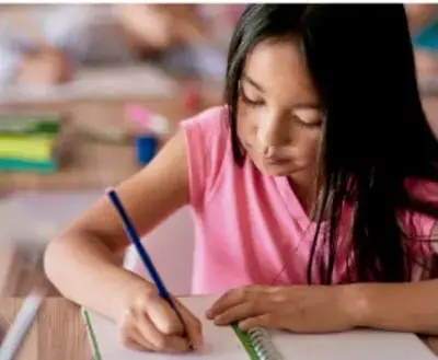 Foto de una niña escribiendo con lápiz en un cuaderno sobre una mesa, ilustrando la elaboración del guion.