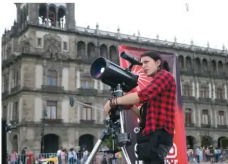 Persona observando con un telescopio frente a un edificio histórico, como ejemplo de divulgación científica.