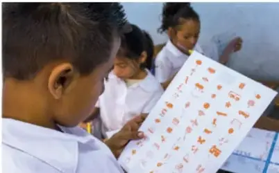 Fotografía de estudiantes de primaria revisando un croquis o mapa sobre una mesa, con apoyo de una maestra.