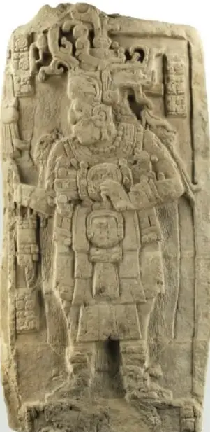 Fotografía de una estela maya de piedra con un gobernante tallado en relieve, con tocado y atavíos; pie: 'Estela maya: bloque de piedra tallado sobre uno o varios de sus lados.'