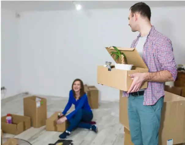 Fotografía de una pareja mudándose a un departamento, con cajas de cartón y una planta, simbolizando la migración hacia la ciudad.