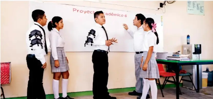 Fotografía de estudiantes de telesecundaria uniformados exponiendo frente al pizarrón donde se lee 'Proyecto Académico 6'.