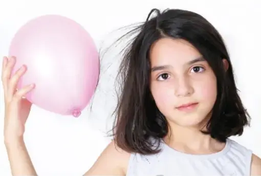 Niña sosteniendo un globo rosa cerca de su cabello, ejemplo de electrización por frotación.