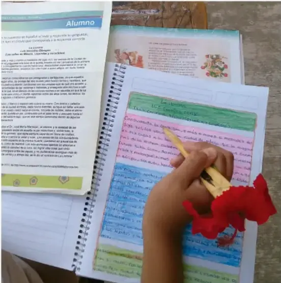 Fotografía de un cuaderno con un resumen escrito a mano con letras de colores (títulos como 'La moldura') junto a libros de texto, mientras una mano escribe con pluma. Crédito: Jesús Eduardo Arteaga Flores, Tamaulipas.