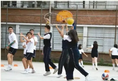 Estudiantes jugando básquetbol en una cancha escolar.