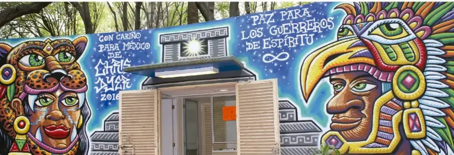 Mural colmado de figuras indígenas y expresiones mexicanas: un jaguar, un rostro con penacho de plumas, un águila con garras, y leyendas como 'Con cariño para México' y 'Paz para los guerreros de espíritu', junto a un año 2018. En el centro se abre una puerta con cortinas.