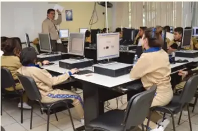 Fotografía de un aula de computación con estudiantes usando equipos de escritorio, relacionada con el acceso a la información digital.